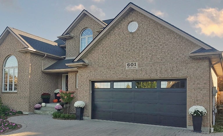 Modern two-story brick home featuring a sleek dark gray double garage door and autumn floral decor.