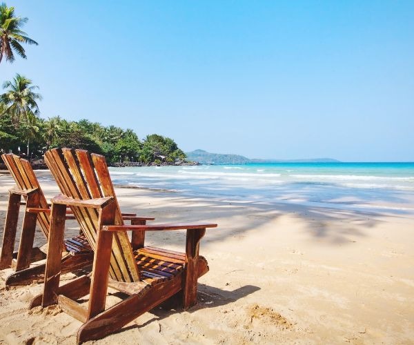 two wooden chairs sitting on a beach