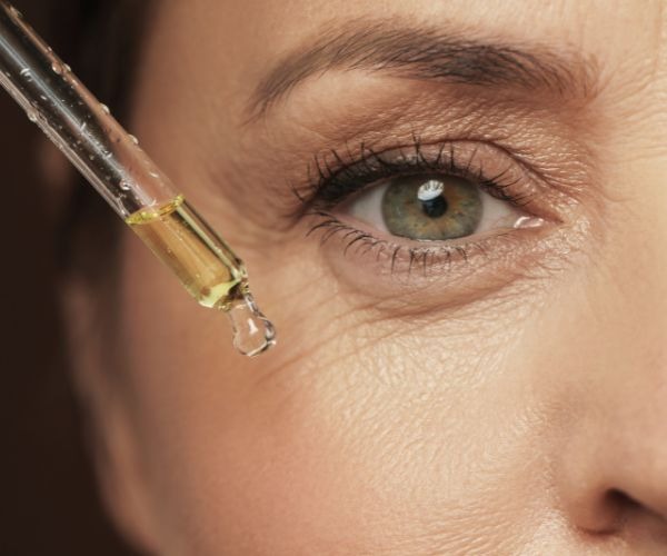 a woman putting serum on her face through a dropper