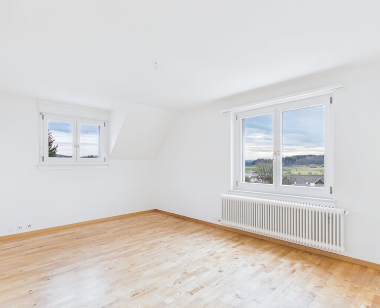 Leerer, moderner Raum mit weißen Wänden, hellem Holzboden und großen Fenstern mit Blick auf ein male