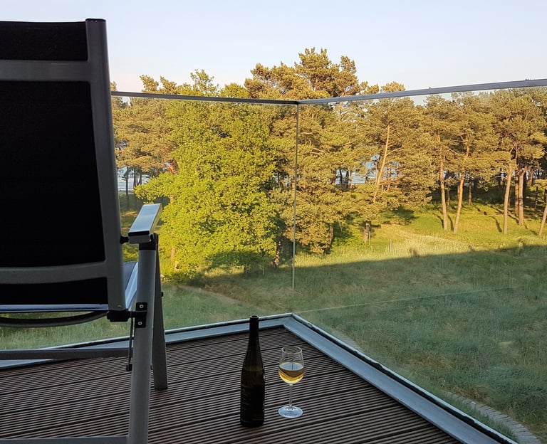 Stuhl mit Blickrichtung Meer steht auf dem Balkon, daneben ein Glas und eine Flasche Wein