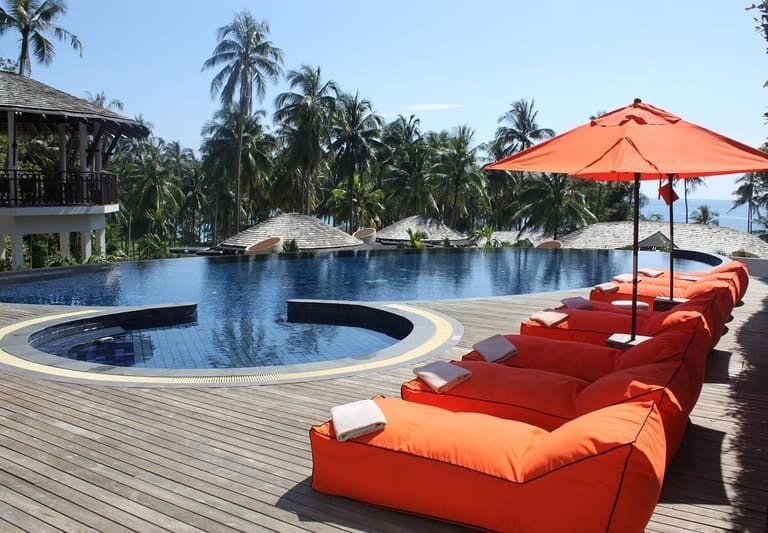 Luxuriöser Infinity-Pool in einem tropischen Resort mit orangefarbenen Sitzsäcken und Blick auf Palm
