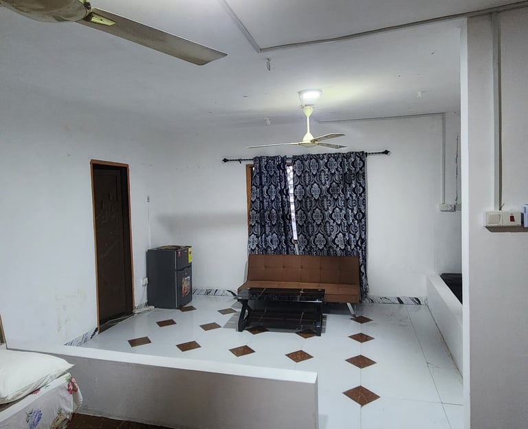 Studio apartment interior with a brown sofa, tiled floor, white walls, and a ceiling fan.
