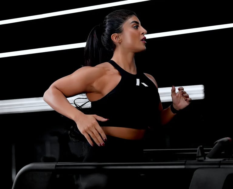 Mais Alhajri running on treadmill in black sportswear inside modern gym with led lights