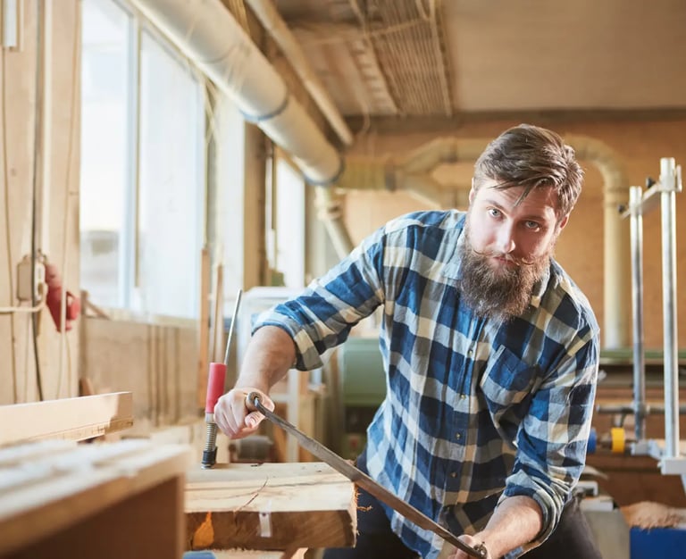a man in a checked shirt is holding a drawknife and working on timber