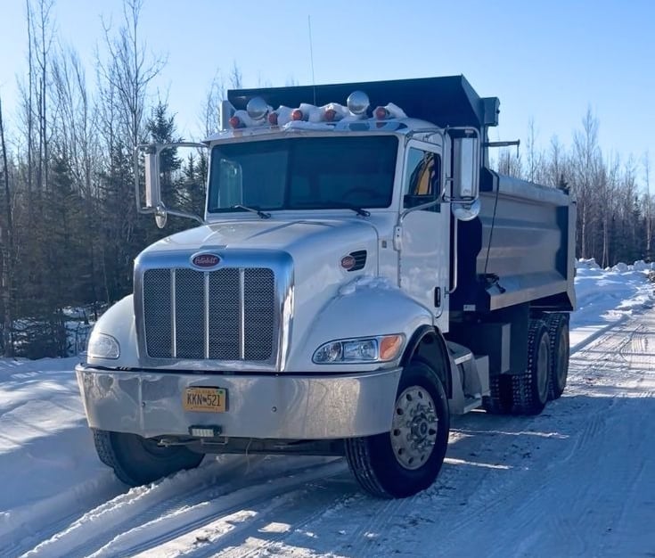 White Peterbilt dump truck parked on a snowy winter road with forest background.