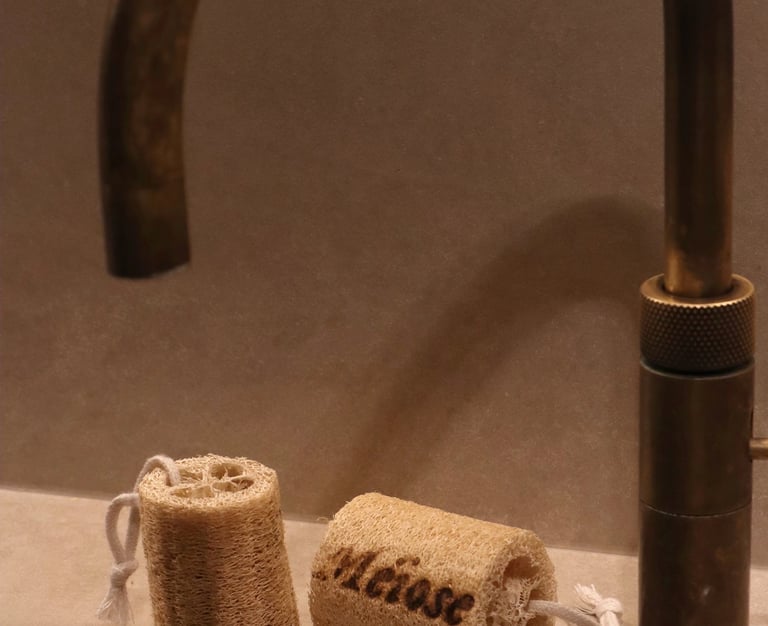 Two natural loofah sponges with cotton loops beside a rustic brass bathroom faucet.