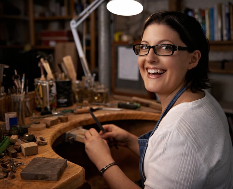 Artesana joyera sonriendo mientras trabaja en su mesa de trabajo con herramientas de joyería