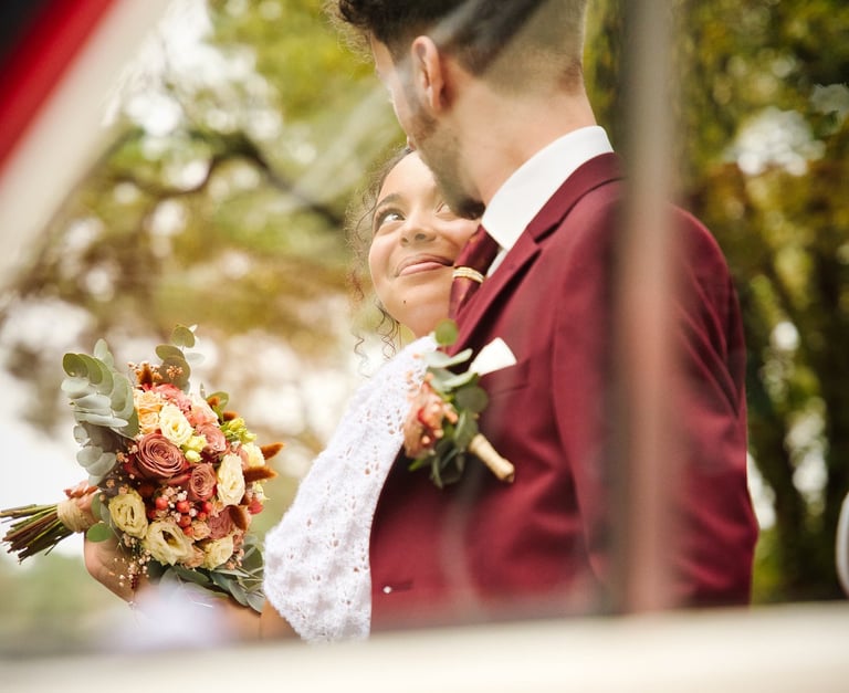 a bride and groom standing in front of a car