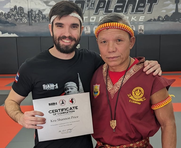 Kru Shannon stands next to Ajhan Suchart after recieving his Kru Certification.