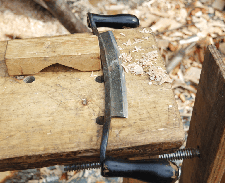 a drawknife with shavings on a piece of timber