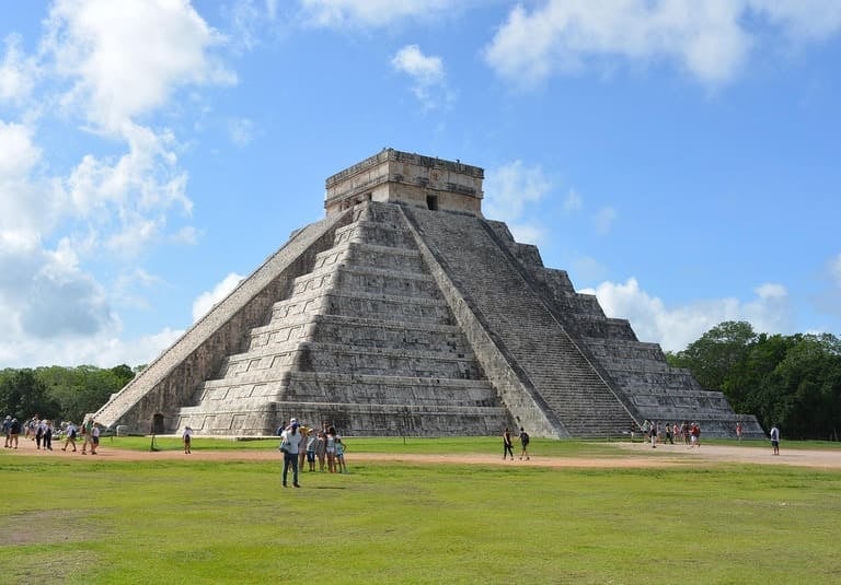 Die antike Maya-Pyramide El Castillo in Chichén Itzá unter blauem Himmel mit Touristen im Vordergrun