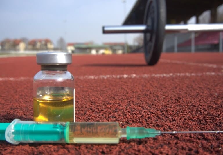 Spritze und Steroid-Fläschchen auf einer Laufbahn mit einer Hantel als Symbol für Doping im Sport