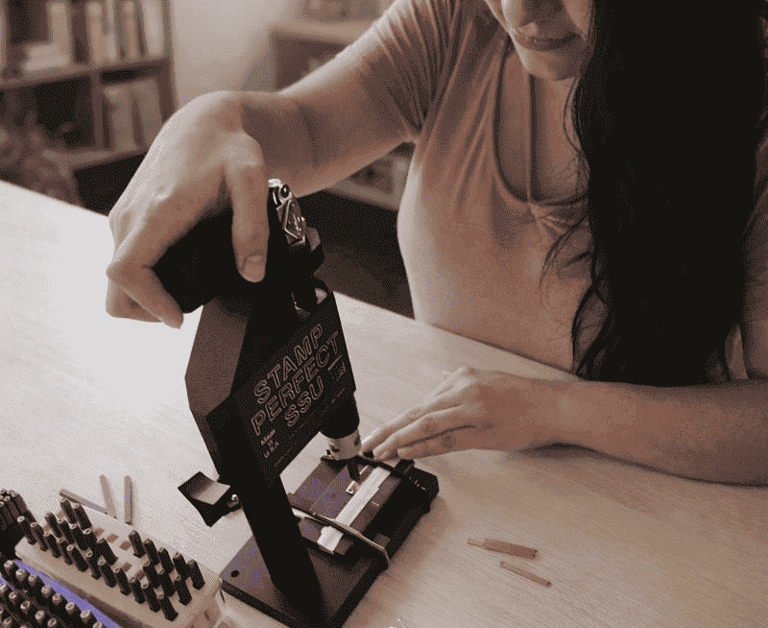 Una mujer utiliza una herramienta de estampado de metal para grabar joyas personalizada