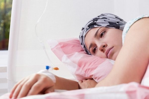 A female cancer patient wearing a headscarf lies in a hospital bed receiving chemotherapy treatment via an IV drip.