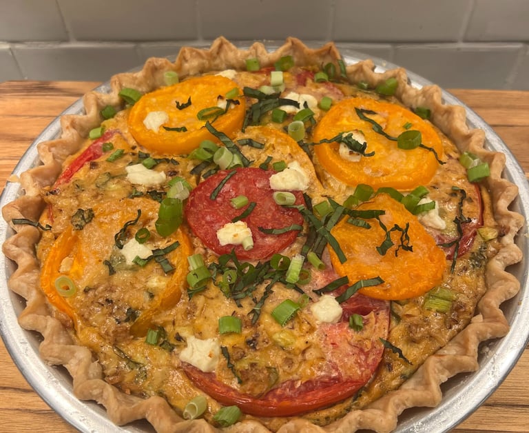 Freshly baked savory tomato pie with yellow and red tomato slices, basil, and scallions in a flaky crust.