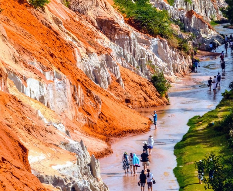 Tourists walking through the Fairy Stream (Suoi Tien) in Mui Ne with red sand cliffs on the left and
