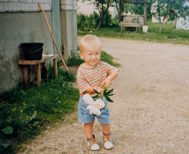 a young boy holding peony blossoms in a driveway