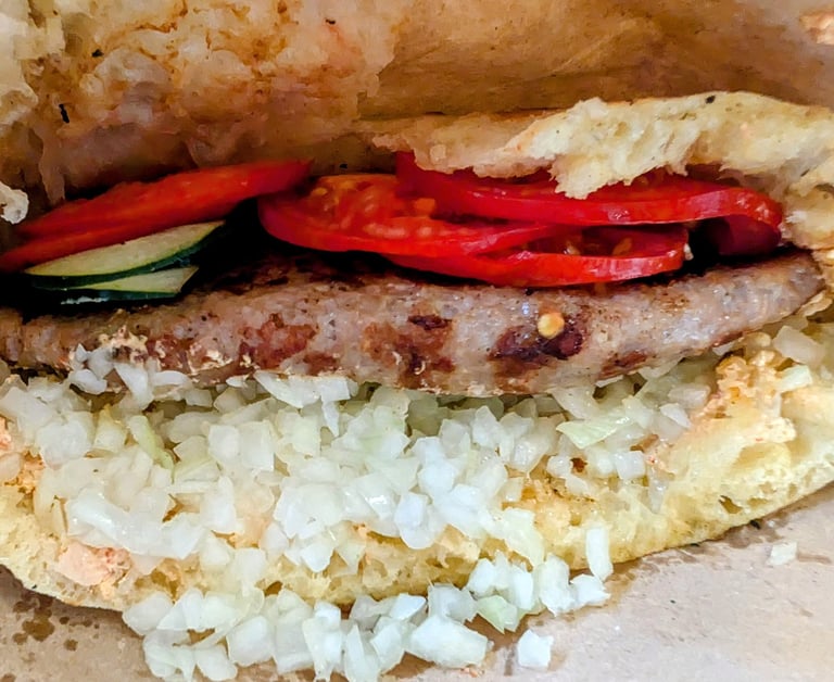 Close-up of a Serbian pljeskavica patty in lepinja bread with onions and tomatoes.