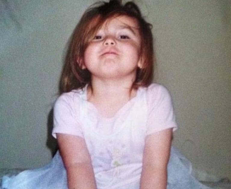 a young girl sitting on a bed with a pink dress