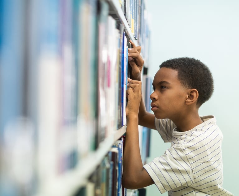 Child with myopia squinting while trying to find a book in the library