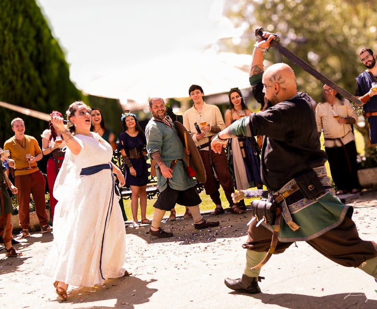 Pareja de novios con vestimenta medieval, ella con vestido blanco y él con traje verde, bailando y l