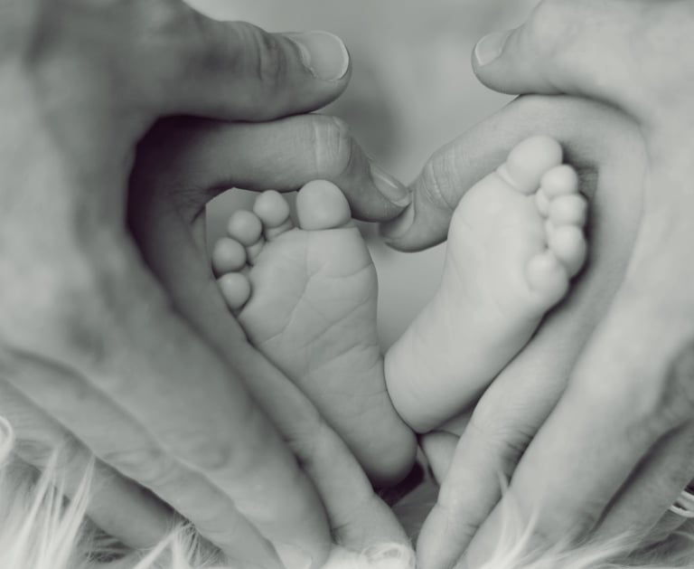 Mãos de mãe e pai segurando os pés de um bebê em formato de coração, simbolizando amor e proteção.