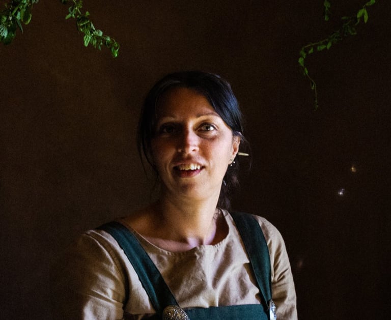 an atmospheric picture of a woman in green viking clothes surrounded by herbal plants