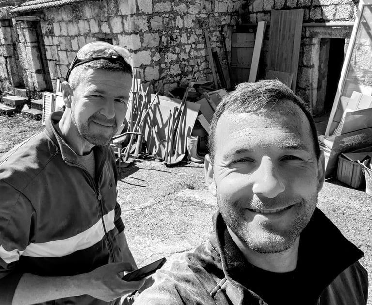 two man are taking a selfie in front of a stone house in dalmatia