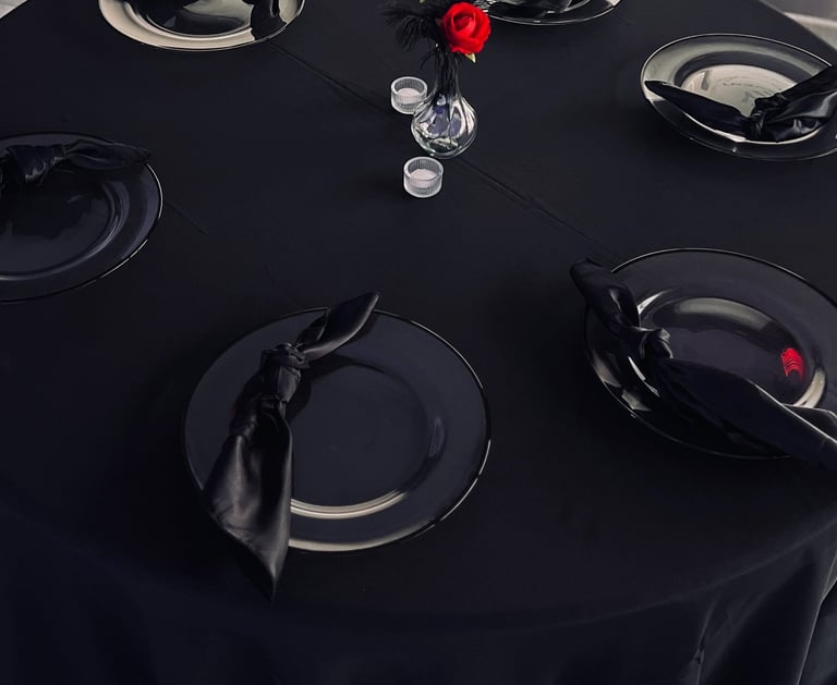 Elegant round table with a black tablecloth, charger plates, black satin napkins, and a centerpiece.