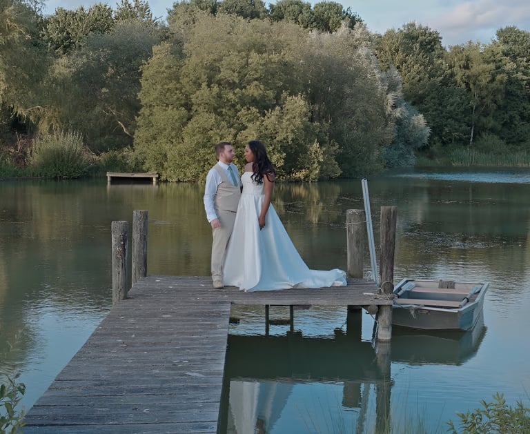 Bride and groom walking along a pier towards a lake.