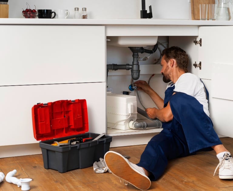 plumber repairing pipes under a kitchen sink in an Auckland home