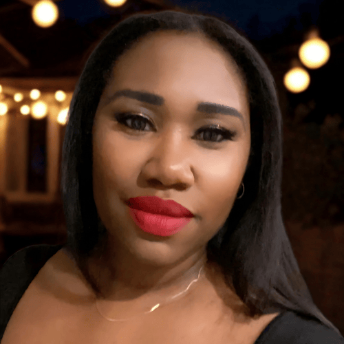 Smiling woman with bold red lipstick and dark hair against a bokeh background of outdoor cafe lights.