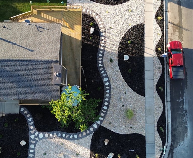 Aerial view of a modern xeriscape front yard featuring decorative black mulch and white gravel patterns.