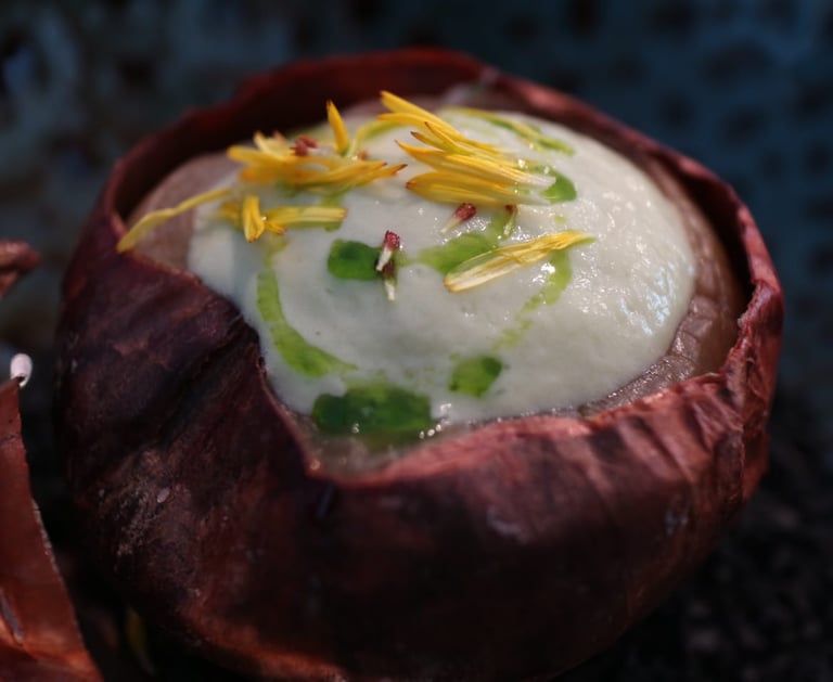 Gourmet onion soup served in a roasted onion skin with creamy foam and edible yellow petals.