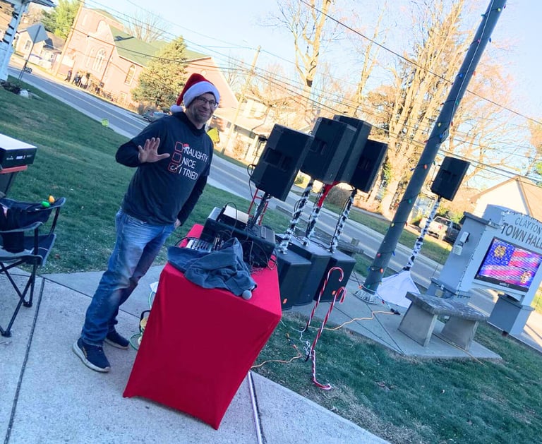 guy in holiday shirt and hat with music equipment waving at the camera