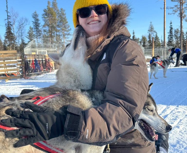a woman in a yellow hat and a husky giving a kiss