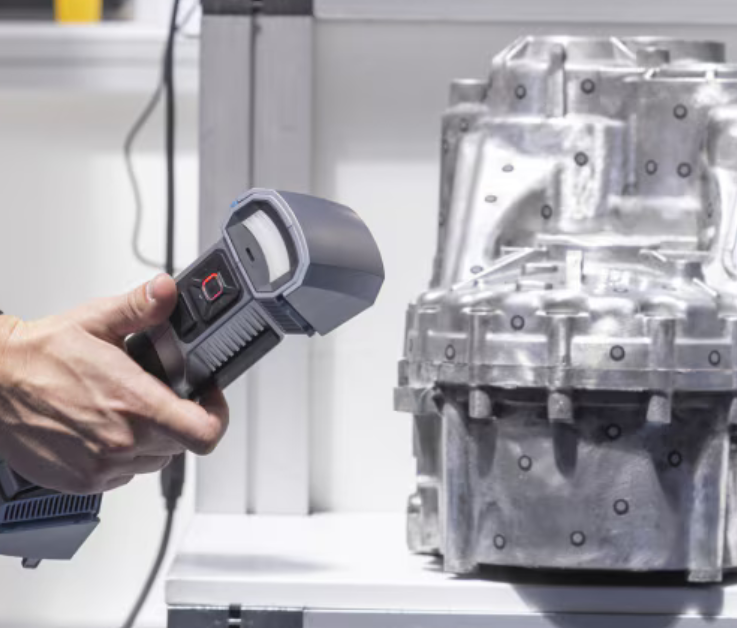 A technician using a portable handheld 3D scanner to digitally capture a complex metal cast engine c
