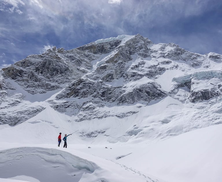 two people standing in the snow near a mountain