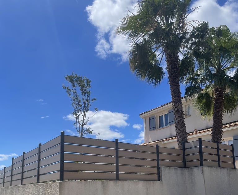 Clôture composite gris clair installée dans un jardin avec palmiers