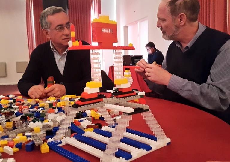 a man and woman sitting at a table with legos Taller Corporasti