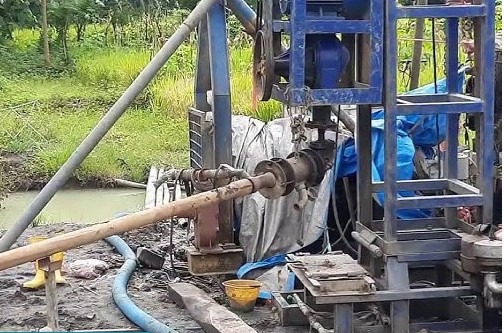 Industrial water well drilling rig operating at an outdoor construction site with pipes and machinery.