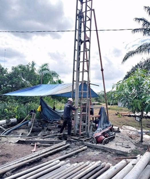 Worker operating a vertical drilling rig for water well construction at an outdoor site.