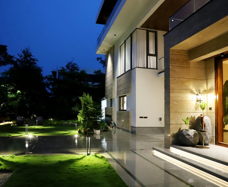 Modern luxury house exterior at night with glowing landscape lighting and manicured garden.