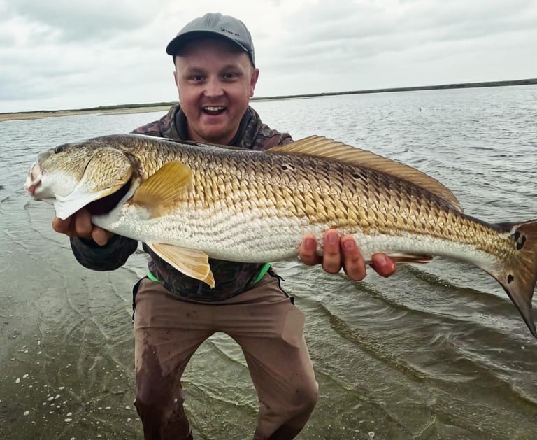 Will Bonniville holding a redfish on the shoreline near the ocean