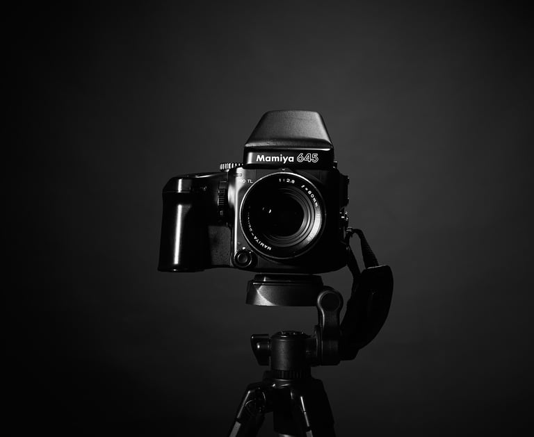 A black and white studio shot of a Mamiya 645 medium format film camera mounted on a professional tripod.
