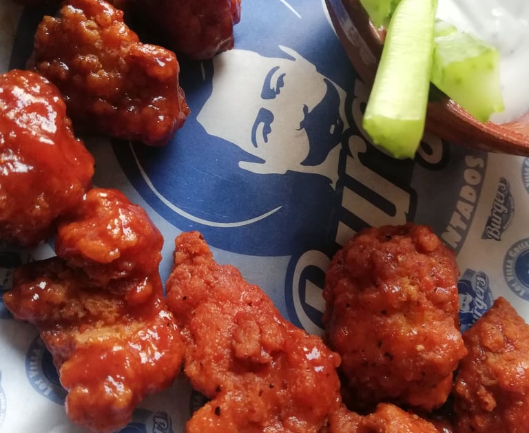 Boneless de pollo bañados en salsa BBQ sobre papel de grado alimenticio, acompañados de aderezo .