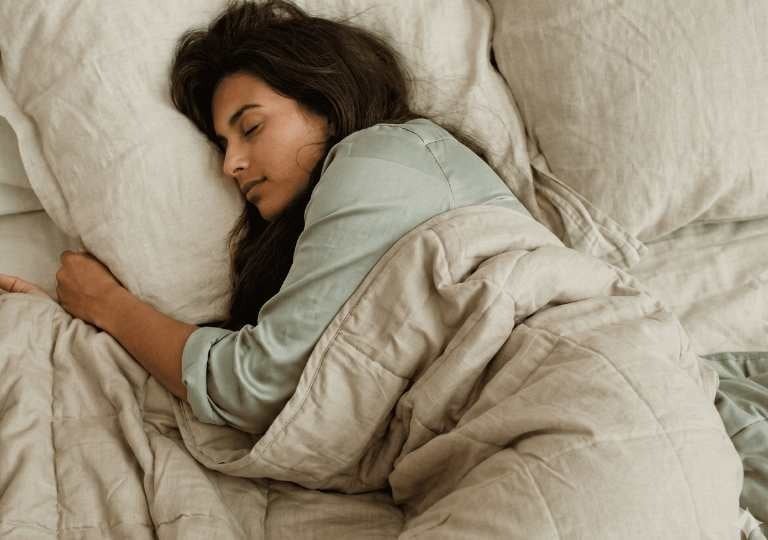 Uma mulher dormindo confortavelmente em uma cama com lençóis macios de linho e um cobertor bege.