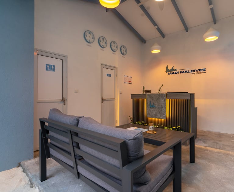 Modern Madi Maldives resort reception desk with lounge seating, world clocks, and ambient lighting.