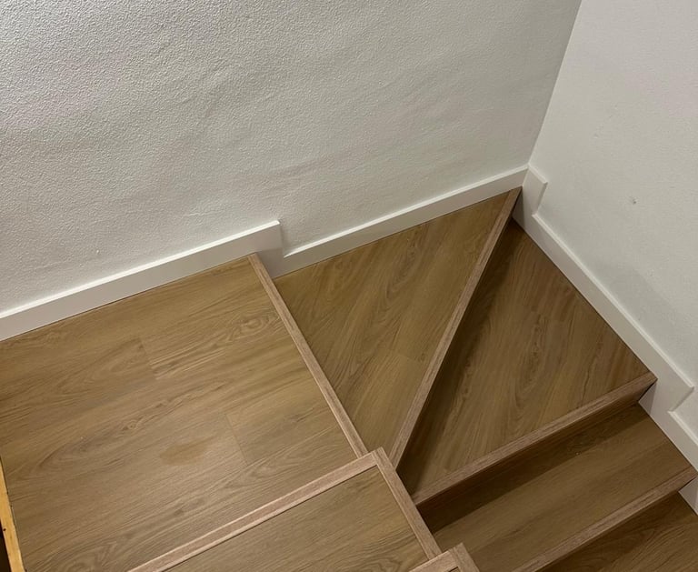 Escalera de madera, tonos claros, pared blanca.